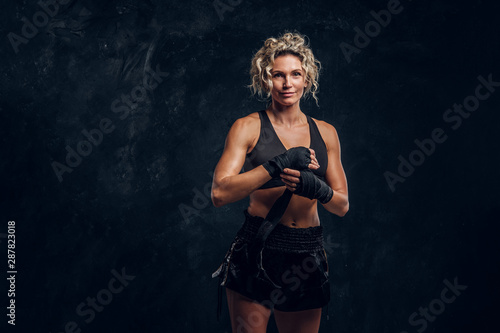 Experienced female boxer is posing for photographer while wearing protective bandages.