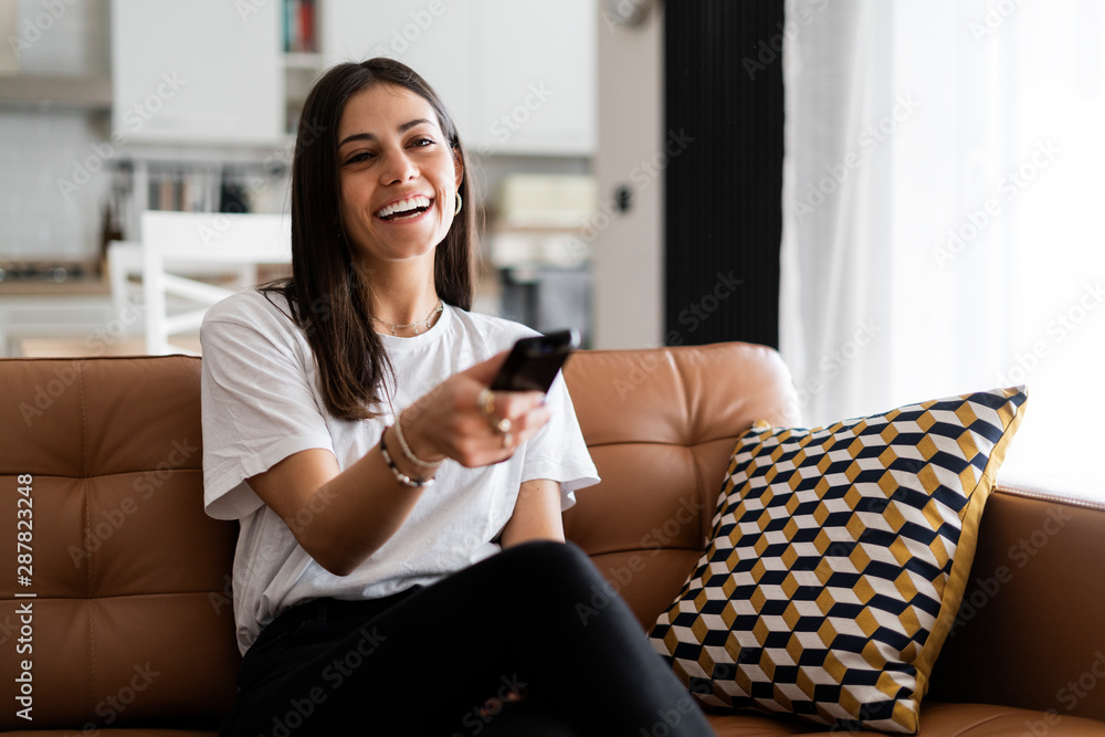 Happy young woman sitting on couch at home watching Tv Happy young woman sitting on couch at home watching Tv