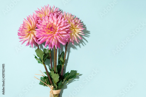 Festive flower bouquet over pastel blue background, copy space. Top view. Creative greeting card with yellow and pink dahlia flowers