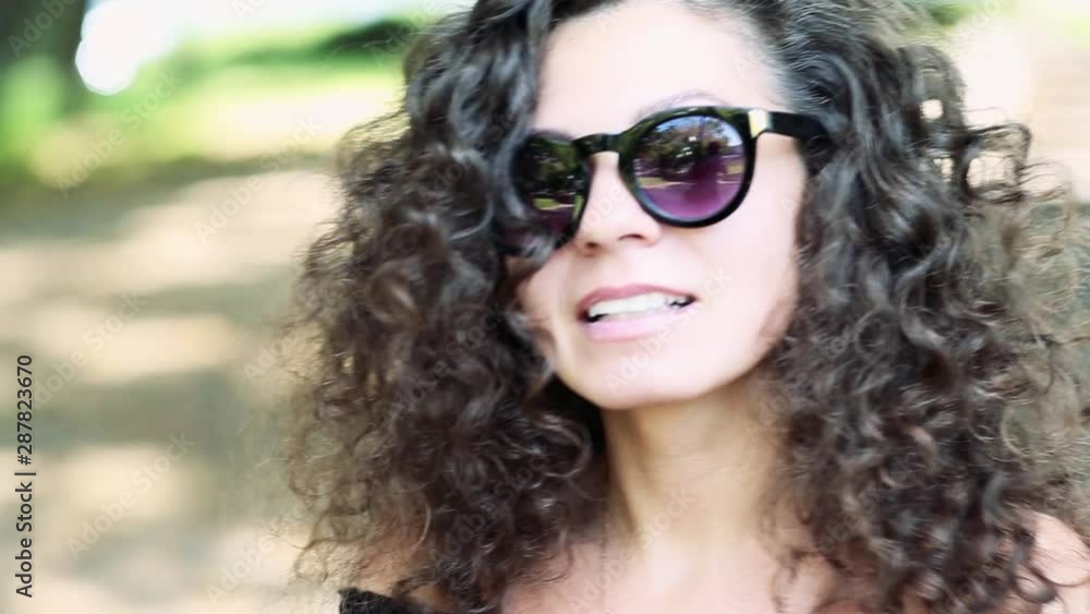 portrait of curly brunette in sunglasses and black dress posing in the city portrait of curly brunette in sunglasses and black dress posing in the city