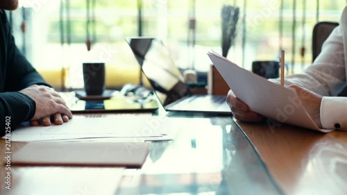 Close-up of mens hands are signing papers and handing them over to colleague in slow motion in interior of light cafe. Negotiations concluded successfully. The contract is signed
