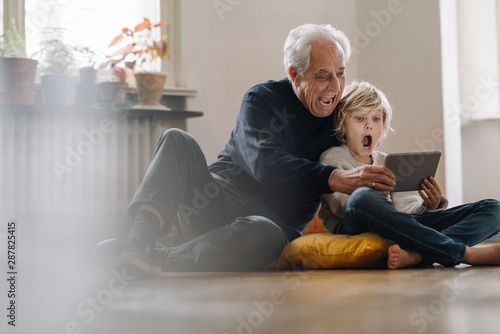 Screaming grandfather and grandson sitting on the floor at home using a tablet photo