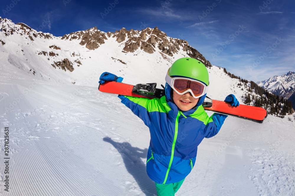 Happy boy carry ski on shoulders walk over slope