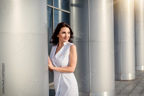 Beautiful middle-eged smiling woman model with dark hair wearing light clothes,posing on the street in summer day 