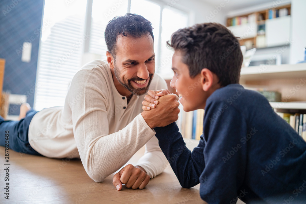 Father and son lying on the floor at home arm wrestling Father and son lying on the floor at home arm wrestling