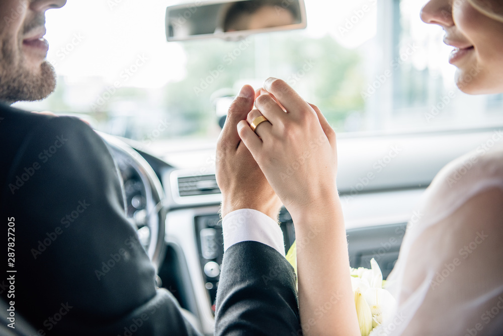 cropped view of bridegroom and bride holding hands in car - obrazy, fototapety, plakaty 