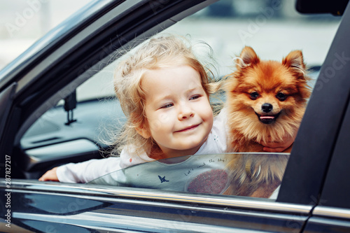 Young pretty girl with cute fluffy dog sitting in car looking trough the window