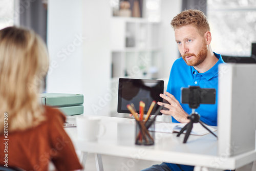 Handsome Caucasian focused employee holding tablet and trying to convince female client to buy stocks.