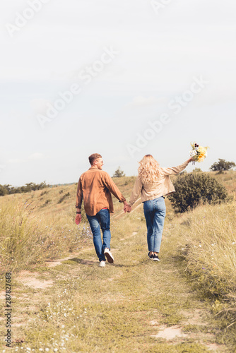 back view of woman with bouquet and man holding hands