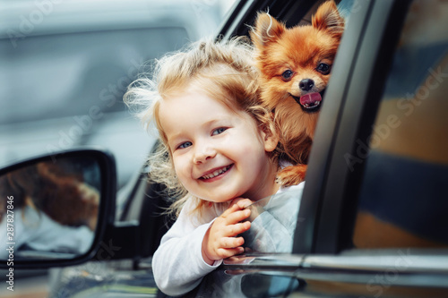 Young pretty girl with cute fluffy dog sitting in car looking trough the window © matilda553
