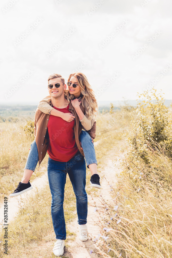 handsome man piggybacking his attractive and blonde girlfriend outside