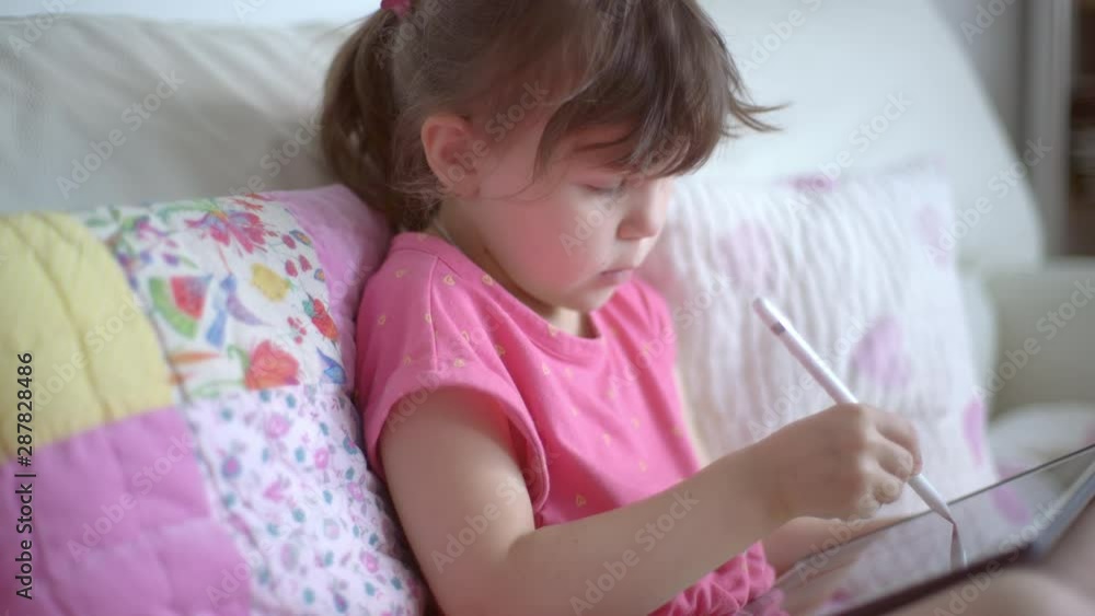 Close-up of a serious focused child draws with a digital pen on a tablet computer. Little beautiful caucasian girl uses gadget for creativity or education Close-up of a serious focused child draws with a digital pen on a tablet computer. Little beautiful caucasian girl uses gadget for creativity or education