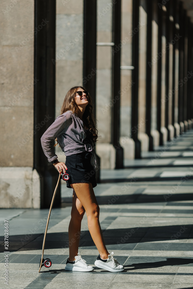 Beautiful young woman with longboard on the city street in sunny weather. Young hipster girl posing with skateboard. Beautiful young woman with longboard on the city street in sunny weather. Young hipster girl posing with skateboard.