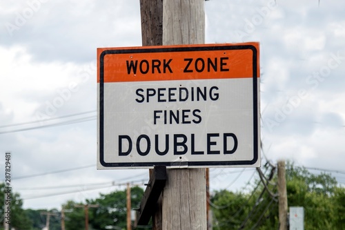 a road sign attached to a electric pole warning drivers about working zone and fine for speeding