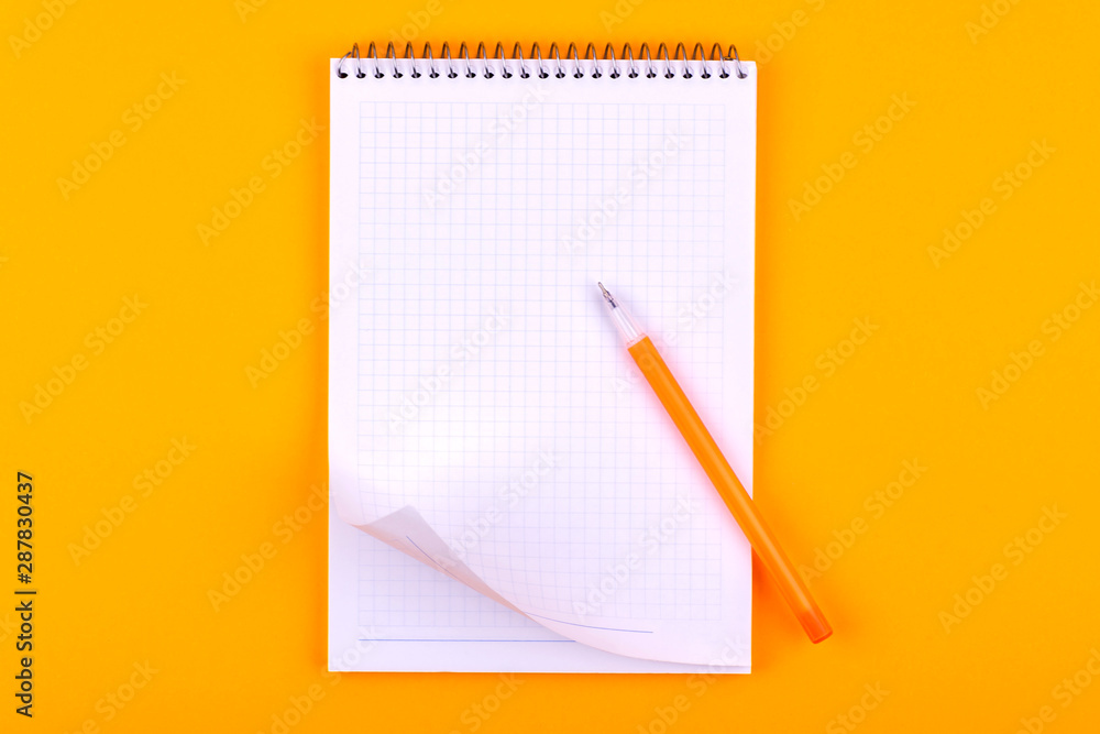 Notebook on a spring with white sheets of paper for drawings, texts and notes, next to a yellow pen lies on an orange background Notebook on a spring with white sheets of paper for drawings, texts and notes, next to a yellow pen lies on an orange background