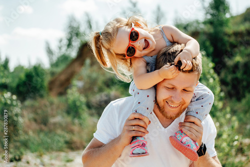 Fotografie Little girl sitting on father's shoulders and laughing.
