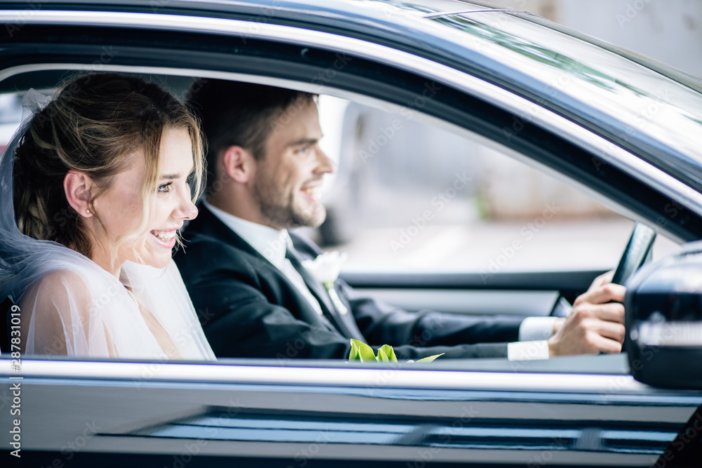 selective focus of attractive bride in bridal veil and bridegroom smiling in car selective focus of attractive bride in bridal veil and bridegroom smiling in car