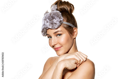 Portrait of young charming woman posing topless in sleeping mask. Beauty concept. Beautiful model with sweet smile looking at camera on white background