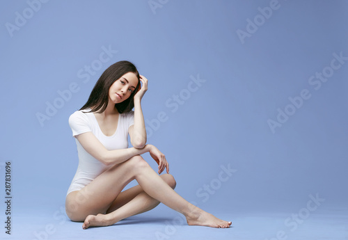 Beautiful slim woman posing in white bodysuit. Fit and sexy woman in underwear swimsuit. Blue background.