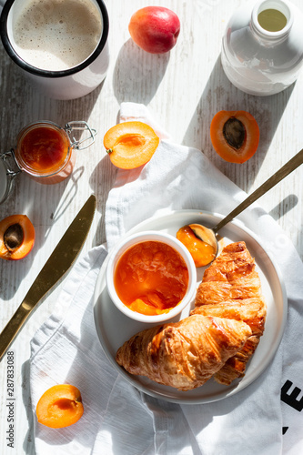 French breakfast with croissant, coffee, apricot jam and apricots. Hard light. Morning.