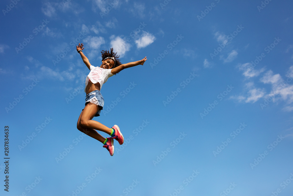 Happy girl in high jump over sky with lifted hands