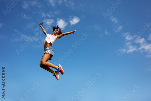 Happy girl in high jump over sky with lifted hands
