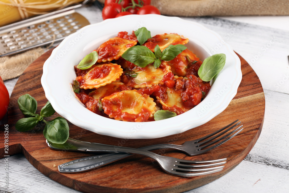 Ravioli with tomato sauce garnished with parmesan cheese and basil on rustic table