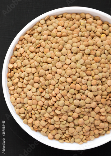 Organic green lentils in a white bowl on a black surface, top view. Flat lay, overhead, from above. Close-up.