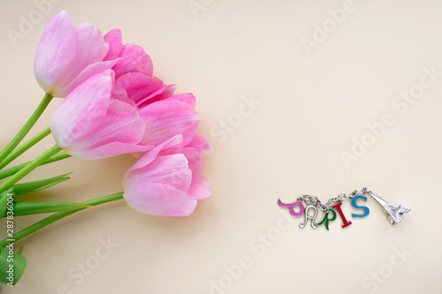 A composition with five buds of pink flowers and keychain similar to the Eiffel Tower with the inscription Paris. Top view on a beige background with space for text