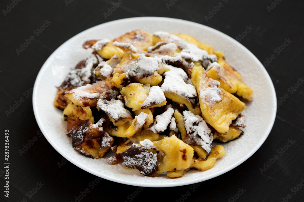 Homemade german Kaiserschmarrn pancake on a white plate on a black background, side view. Homemade german Kaiserschmarrn pancake on a white plate on a black background, side view.