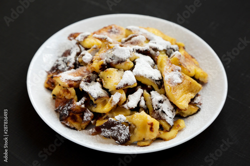 Homemade german Kaiserschmarrn pancake on a white plate on a black background, side view.
