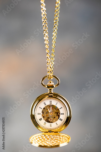 Vintage pocket watch hanging on a chain. Roman numerals on the dial.