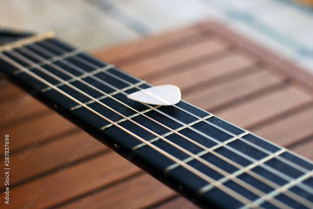Obraz premium Guitar pick on the fingerboard of a brown guitar.