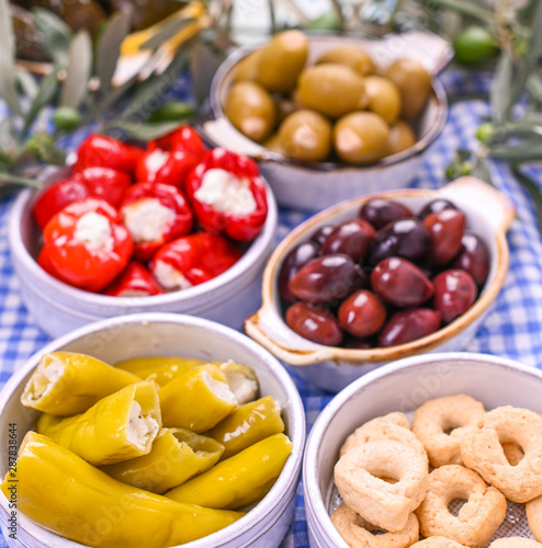 Traditional appetizers, green and red olives from Greek cuisine. Fresh branches of olives. Copy space. Blue checkered tablecloth.
