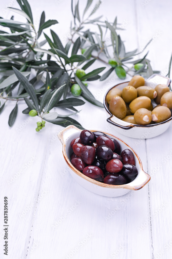 Naklejka Traditional appetizers, green and red olives from Greek cuisine. White wood background. Fresh branches of olives. Copy space.