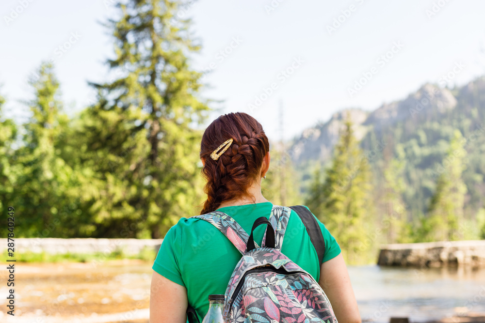woman traveler with backpack looking at amazing mountains and forest, wanderlust travel concept, space for text, atmospheric epic moment