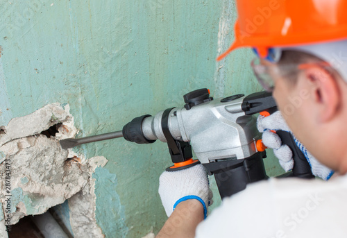 The builder is making hole in wall at construction site with hammer drill perforator equipment.