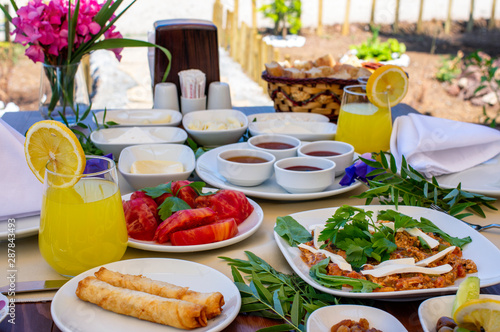 A breakfast table composed of fried egg with cheese, orange juice, tomato salad and various marmalades