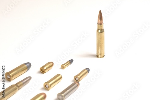 A large bullet (7.62 x 51mm NATO) standing in front of several smaller bullets laying over a white surface