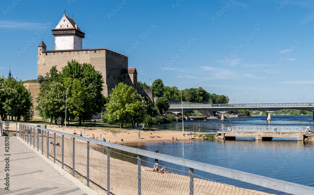 Narva or Hermann castle on a sunny day and the river with sunbathers