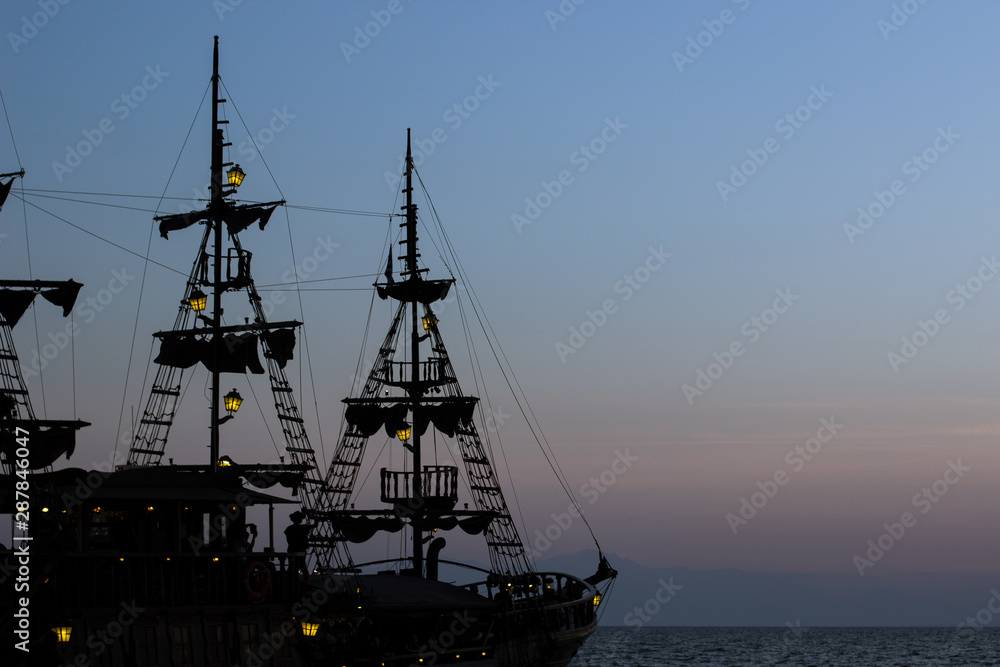 moody cruise vacation picture of vintage medieval ship mast silhouette with lanterns yellow illumination in evening twilight romantic lighting above the sea, copy space 
