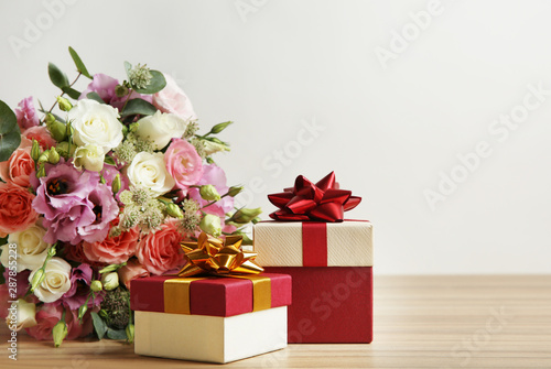 Beautiful bouquet of flowers and gift boxes on wooden table against light background. Space for text