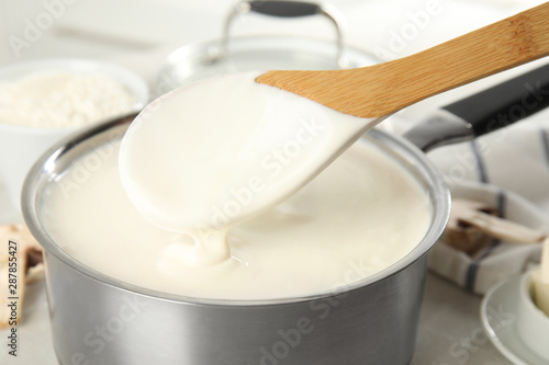 Spoon and pan with delicious creamy sauce, closeup view