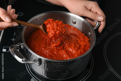 Woman cooking delicious tomato sauce in pan on stove, closeup