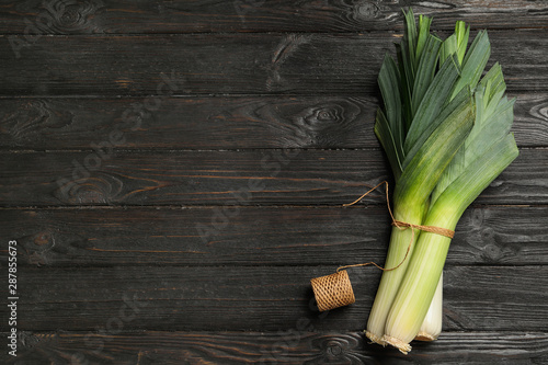 Fresh raw leeks on black wooden table, flat lay with space for text. Ripe onion