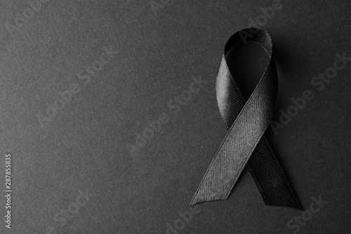 Black ribbon on dark background, top view with space for text. Funeral symbol