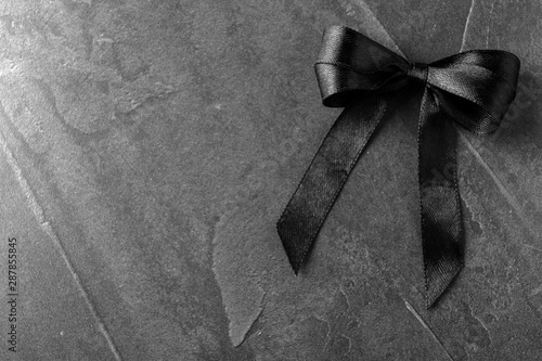 Black ribbon bow on dark grey stone surface, top view with space for text. Funeral symbol photo