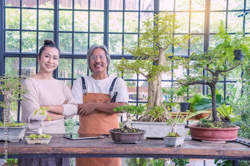 Asian senior couple, the tree shop owner, opened and happy professional  bonsai tree smiling to the camera and  posing in his greenhouse 