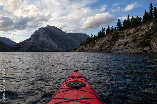 Kayaking in Glacier Lake surrounded by the beautiful Canadian Rocky Mountains during a cloudy summer sunset. Taken in Upper Waterton Lake, Alberta, Canada.