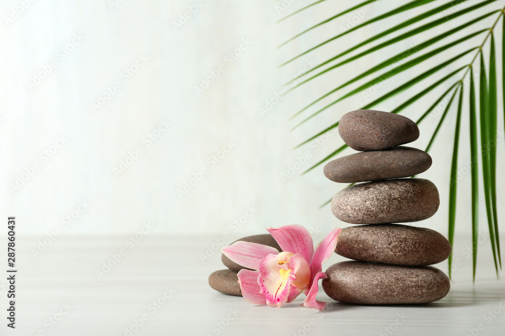 Obraz premium Stack of spa stones, palm leaf and flower on table against white background, space for text